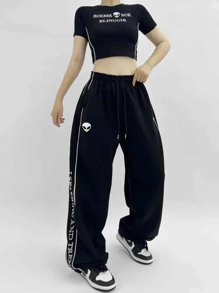 Front view of model wearing black American style printed sweatpants with white lettering