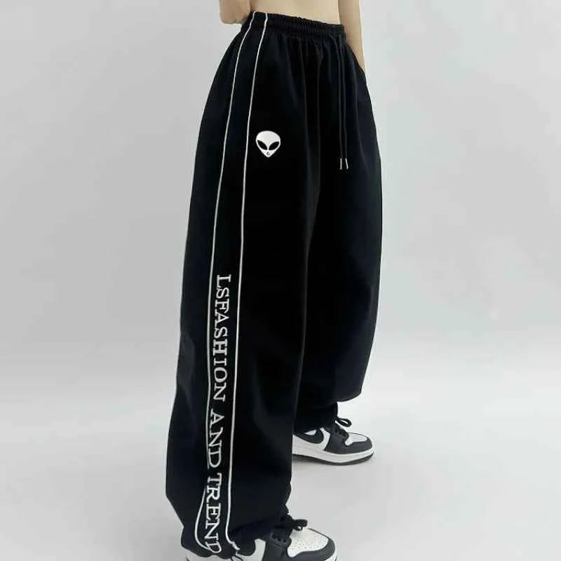 Front view of model wearing black American style printed sweatpants with white lettering