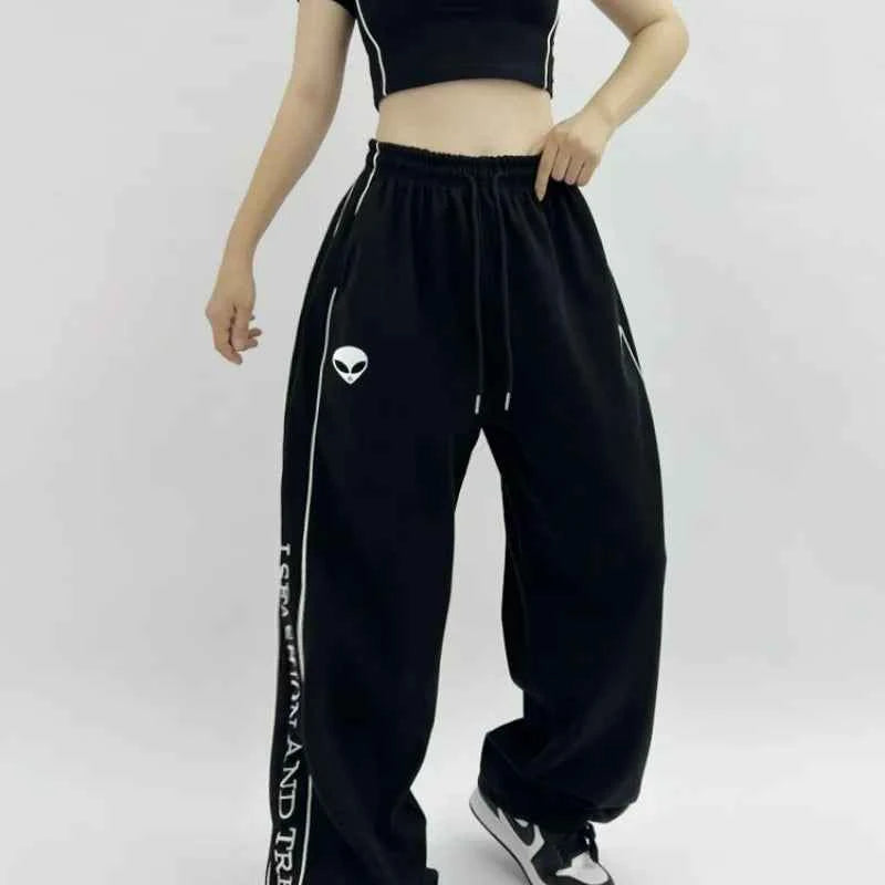 Front view of model wearing black American style printed sweatpants with white lettering