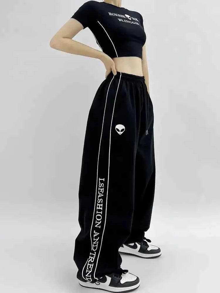Front view of model wearing black American style printed sweatpants with white lettering